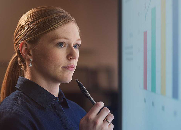 A female student holding a pen to her chin while analyzing data