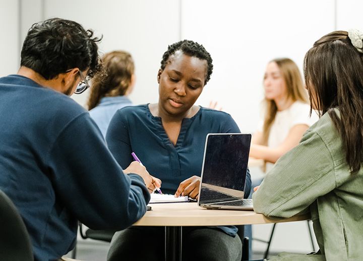 3 students sitting in a round table talking and writing information down